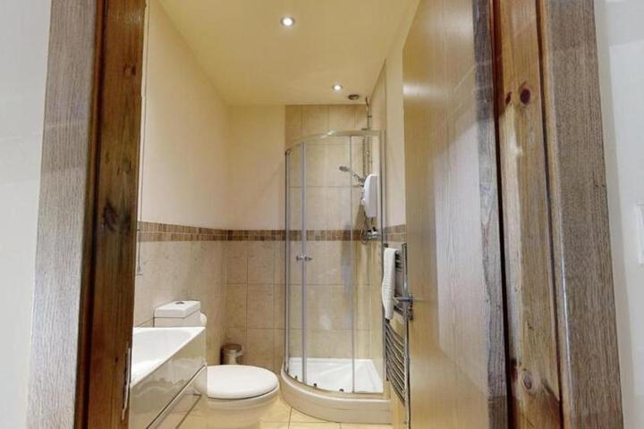 Cozy bathroom in The Horse & Farrier, Otley, features tiled walls, a glass shower, wooden door, and modern fixtures.