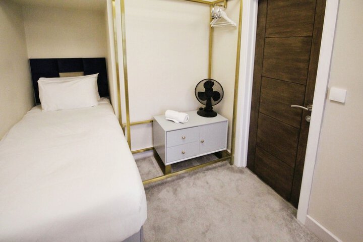 Single bed room at The Psalter, Nether Edge, with beige walls, wooden door, small fan, and light grey furnishings.